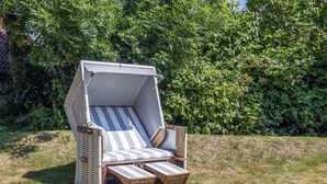 A beach chair with a canopy, positioned on a grassy area with a dense green hedge in the background.