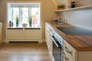 Une cuisine dotée de plans de travail en bois, d’un four encastré et d’une fenêtre ornée de plantes sur le rebord.