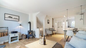 Amplia sala de estar con piso de madera, un sofá, una mesa de centro y una chimenea. Hay un comedor con una mesa y sillas, y una cocina al fondo.