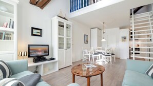 Un salon spacieux équipé d’un téléviseur, d’une table basse en bois et d’un coin repas avec des meubles blancs.