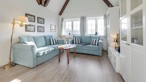 Un salon avec un canapé bleu clair, une table basse en bois et un lampadaire. Des tableaux encadrés ornent le mur, et une fenêtre est agrémentée de rideaux.