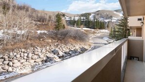 A balcony with a view of a mountainous landscape, a stone wall, and a building with a beige facade. - Saint James Place 335 (Beaver Creek)