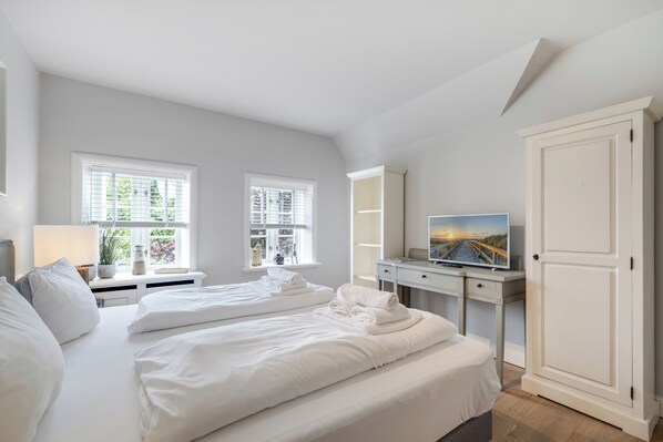 A bedroom with a large bed, two bedside tables, a desk with a TV, and a wardrobe. - Großzügig Geschnittene Og-wohnung im Historischen Kern von Keitum (Sylt / OT Keitum)