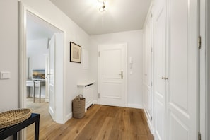 A hallway with wooden flooring, white walls, a door, a framed picture, and a basket. - Großzügig Geschnittene Og-wohnung im Historischen Kern von Keitum (Sylt / OT Keitum)