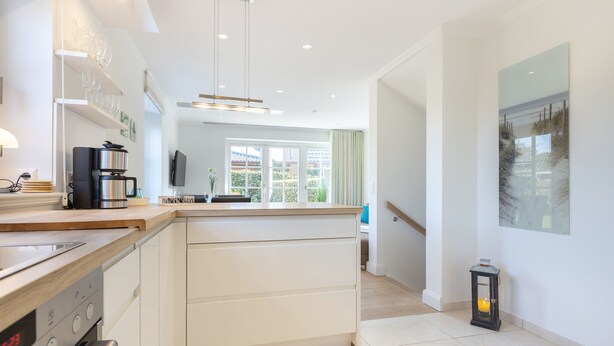 A modern kitchen with a central island, built-in oven, and a coffee maker. - Gode Tiet - Schöner Neubau im Herzen von Westerland (Sylt / OT Westerland)