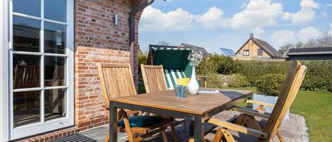 A patio with a wooden table and chairs, a white vase, and a green chair.