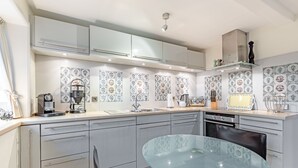 A modern kitchen with grey cabinets, a glass table, and patterned backsplash tiles. - Restauriertes, Unter Denkmalschutz Stehendes Reetdach-einzelhaus der Extraklasse (Sylt / OT Keitum)