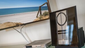 A television set on a glass table with a beach view through a window. - Restauriertes, Unter Denkmalschutz Stehendes Reetdach-einzelhaus der Extraklasse (Sylt / OT Keitum)
