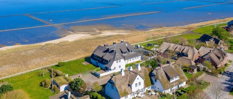 An aerial view of a coastal village with thatched-roof houses, a sandy beach, and a large body of water.
