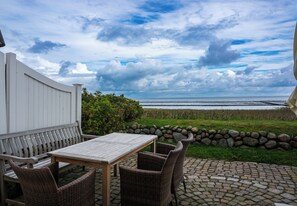 A patio with a table and chairs, overlooking a beach and ocean.