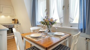 Un comedor con una mesa de madera dispuesta para cuatro personas, sillas blancas y un jarrón con flores.