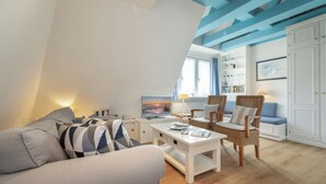 Una sala de estar moderna con un sofá, una mesa de centro y un sillón. Hay una estantería y un televisor al fondo.