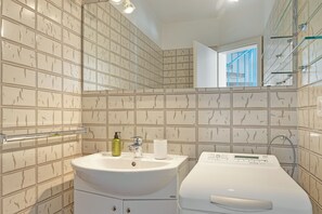 A bathroom with a white sink, a mirror, and a white washing machine.