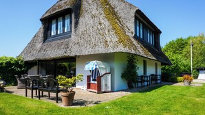 Une maison à toit de chaume dotée d’un espace extérieur aménagé et couvert, ainsi que d’une pelouse.