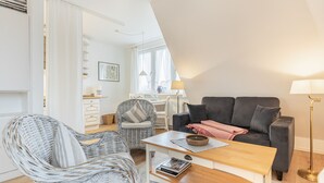 Un salon moderne avec un canapé gris, des fauteuils en osier, une table basse en bois et un bureau avec une lampe.