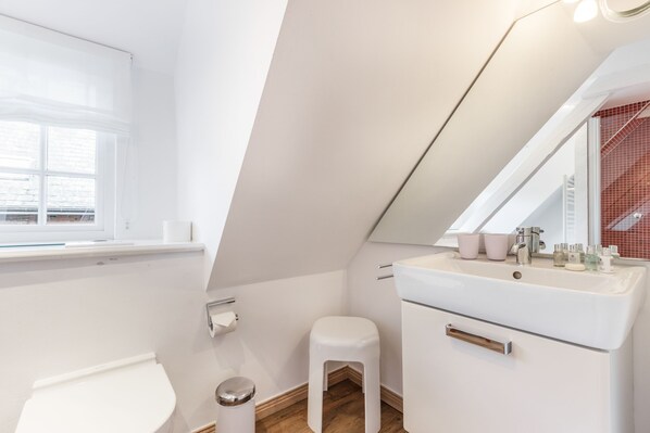 A modern bathroom with a white sink, a toilet, and a small stool. - Gookis Hüs - Idyllisches Friesenhaus in Keitum (Sylt / OT Keitum)
