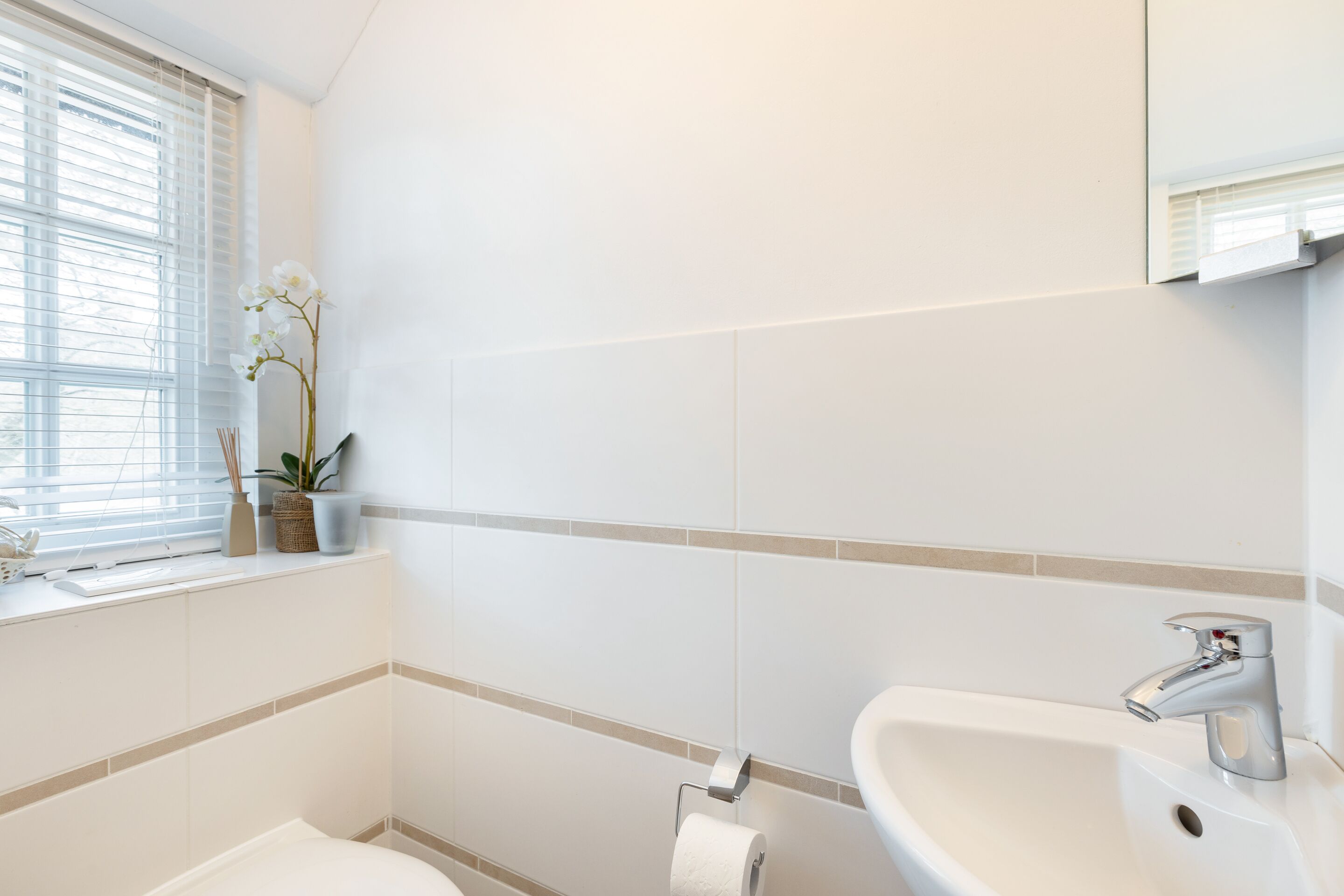 Une salle de bain avec des toilettes, un lavabo et une fenêtre équipée de stores.