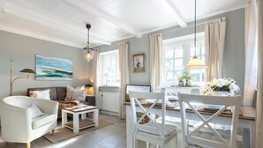 Un salon bien éclairé, avec un canapé blanc, une table à manger et une chaise blanche. Il y a un tableau au mur et une lampe sur la table.