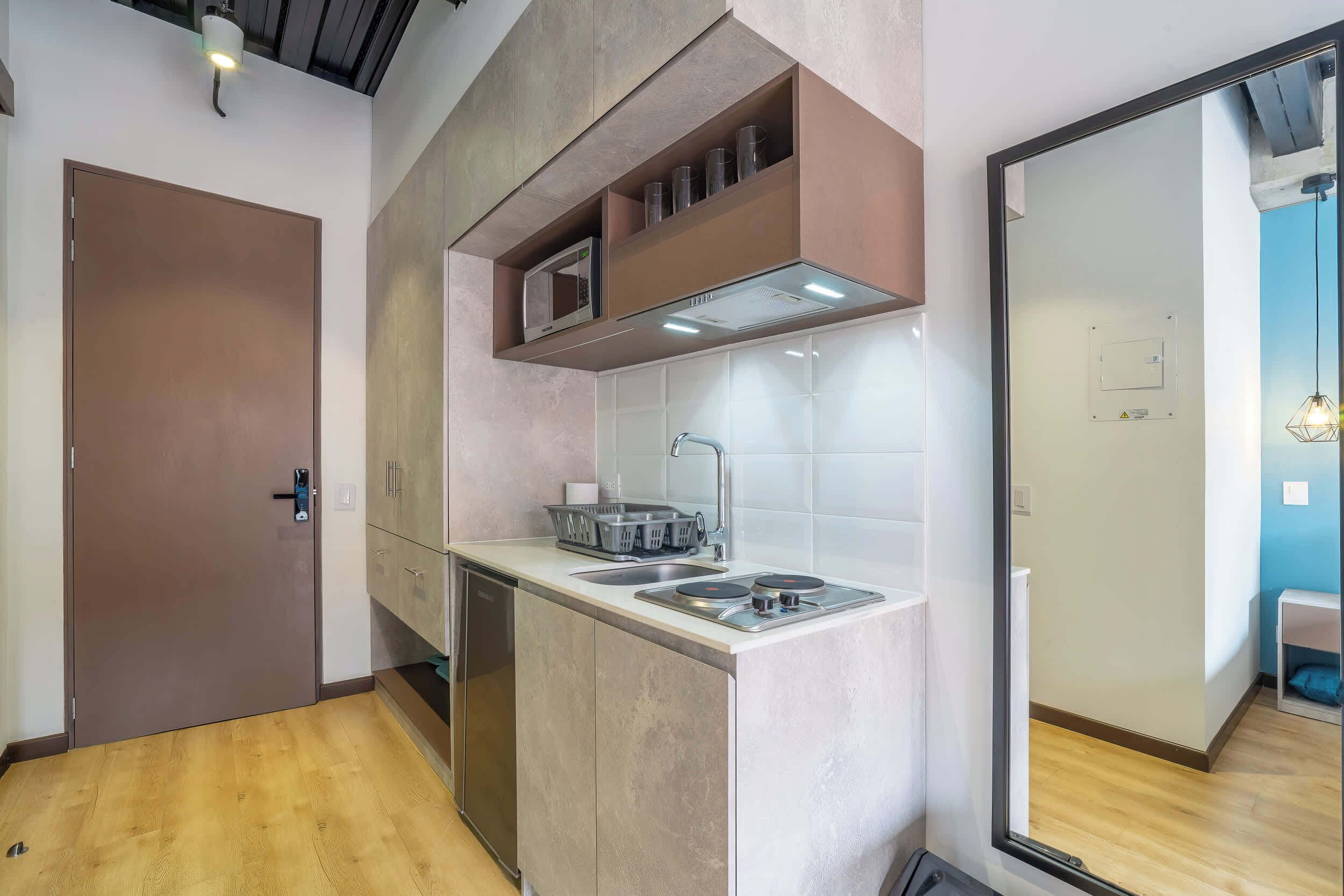 Une cuisine compacte équipée d’un four à micro-ondes, d’un évier et d’une cuisinière, avec un plancher en bois et une porte située sur le côté gauche.