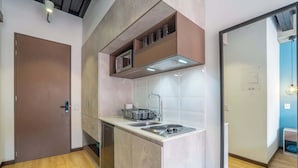 Une cuisine compacte équipée d’un four à micro-ondes, d’un évier et d’une cuisinière, avec un plancher en bois et une porte située sur le côté gauche.
