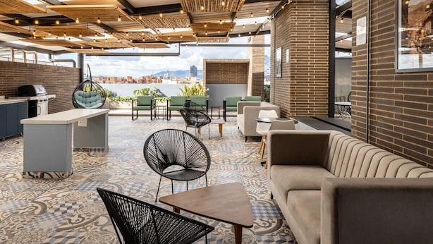 Un bar situé sur le toit d’un immeuble, offrant une vue sur la ville, avec différents types de sièges et un espace bar.