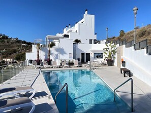Ein moderner Poolbereich mit Liegestühlen, einem Pool und einem Gebäude mit Balkonen.