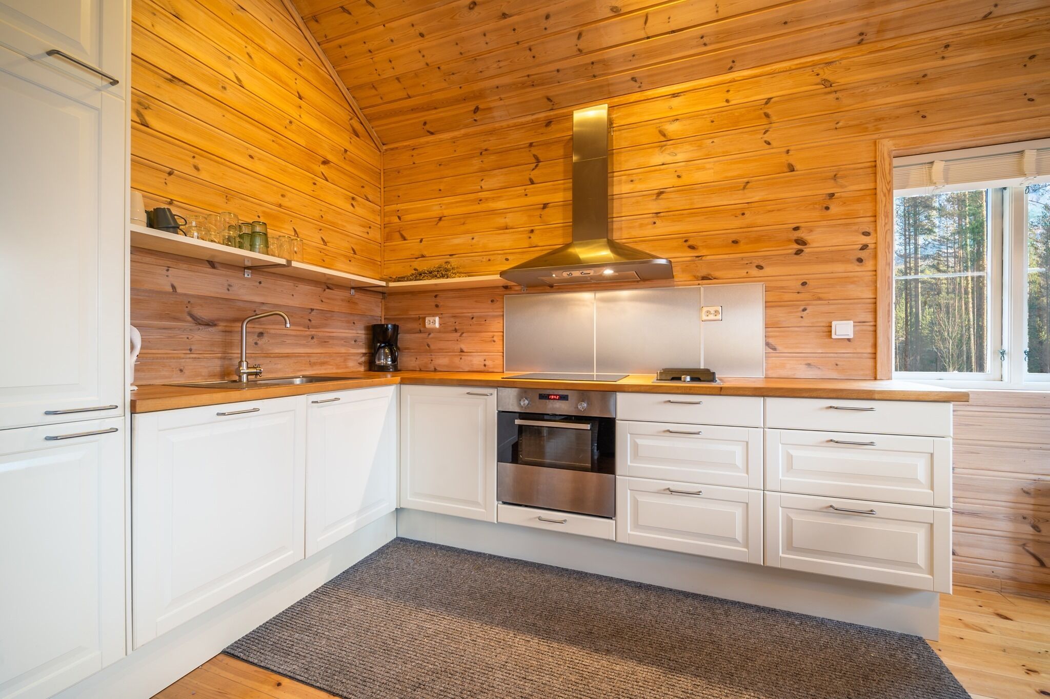 A modern kitchen with wooden paneling, white cabinets, stainless steel appliances, and a large window.