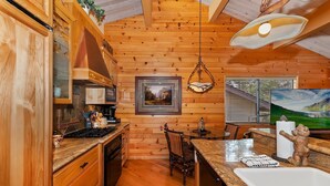 Interior de una cabaña de madera con cocina, comedor y un amplio ventanal con vistas a la montaña.