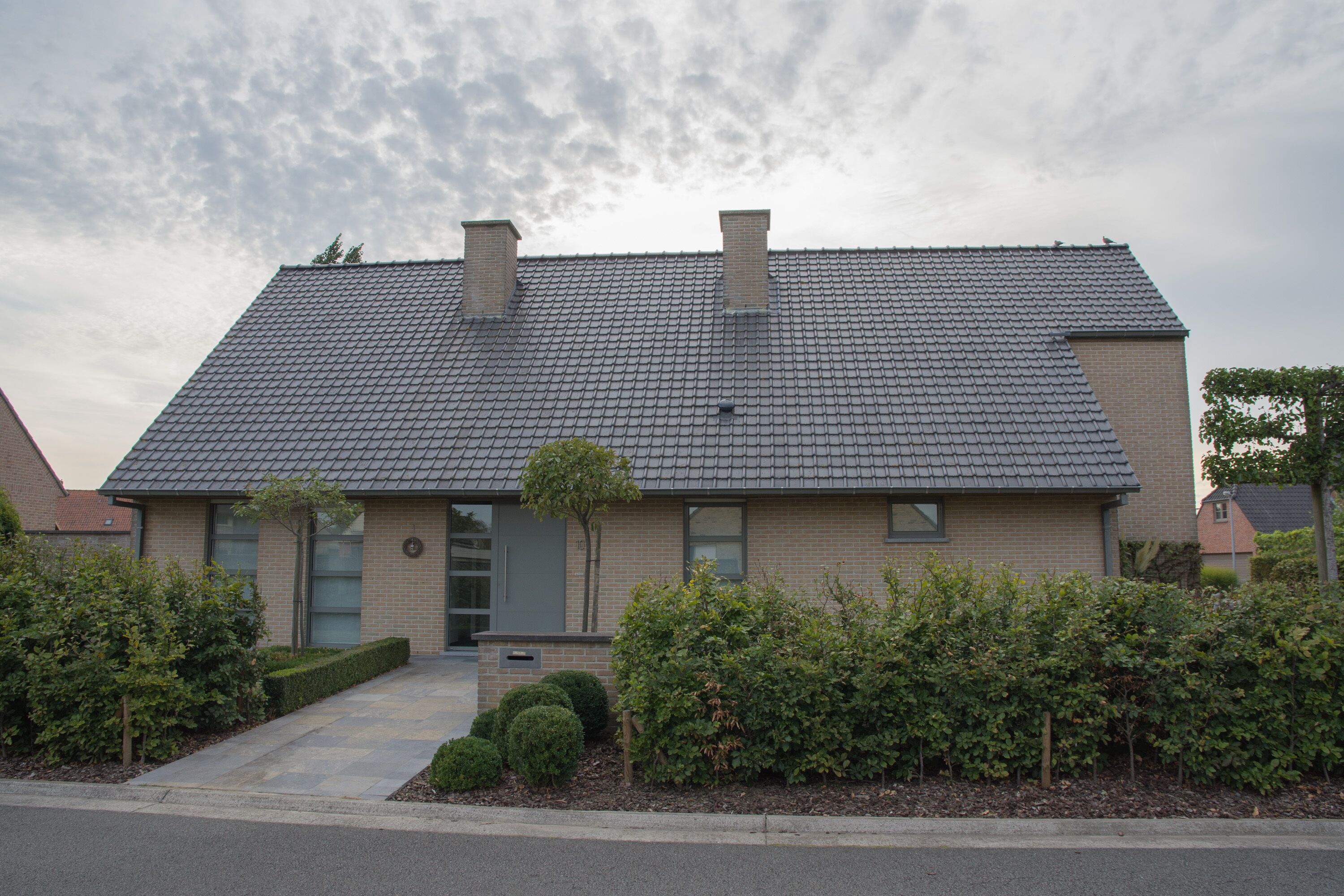 A two-story house with a tiled roof, a front entrance, and a small front yard with trimmed bushes.