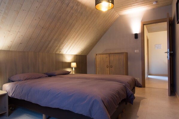 A bedroom with two beds, wooden ceiling, and a door leading to another room.