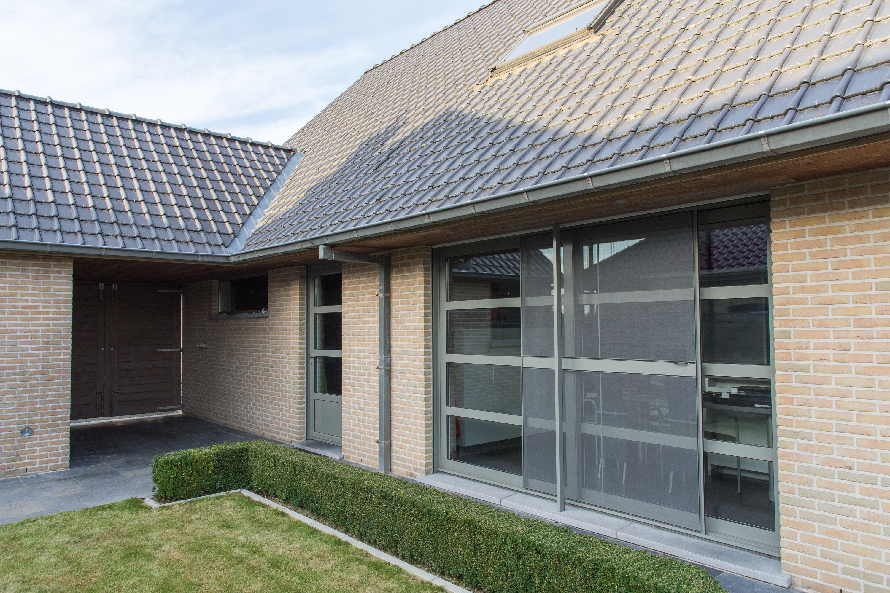 Een modern gebouw met een pannendak, grote ramen en een gevel van baksteen.