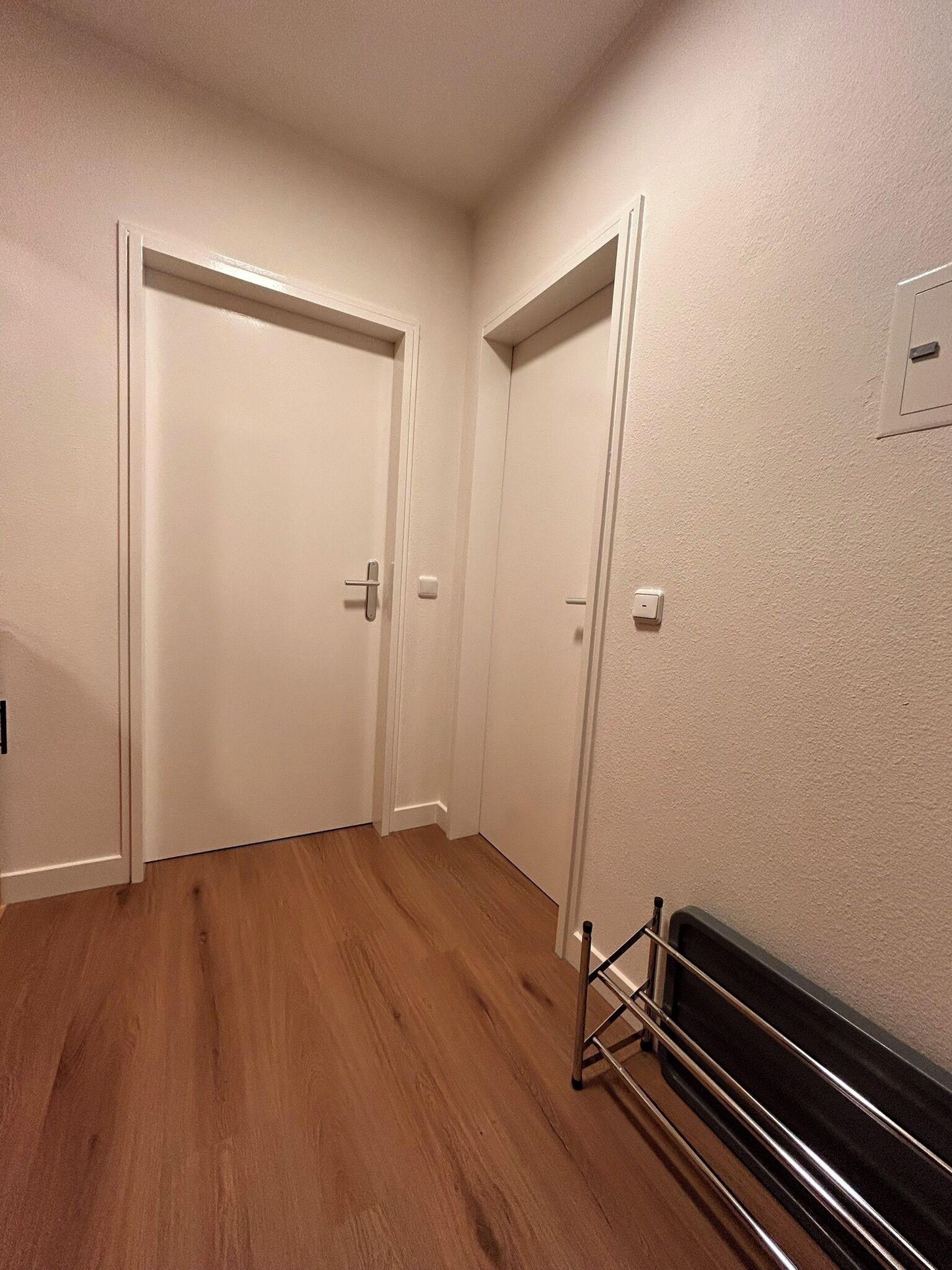 A hallway with wooden flooring, white doors, and a radiator on the right.