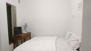 Une petite pièce propre, avec un lit, un bureau et un ventilateur.