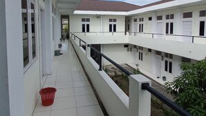 Un couloir au sol carrelé, un panier rouge et un balcon avec une balustrade.