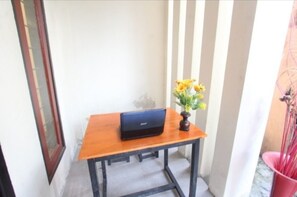 A small wooden table with a laptop and a vase of yellow flowers on a balcony.