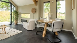 A modern dining area with a round table, six chairs, and a large window offering a view of greenery.