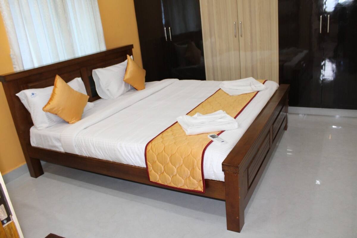 A neatly made bed with white linens and a gold accent, a wooden headboard, and a large wardrobe with a mirror.