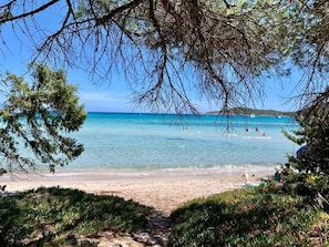 A beach with clear water, people swimming, and a path leading to the shore. - S'échapper Pour des Vacances de Rêves (Linguizzetta)