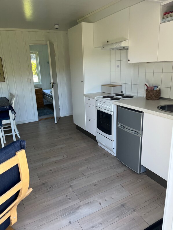 A compact kitchen with white cabinetry, a stove, oven, and dishwasher. A dining area with a table and chairs is visible in the background.