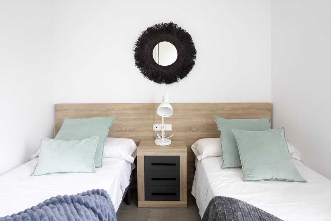 A bedroom with two beds, a nightstand, a mirror, and a lamp.