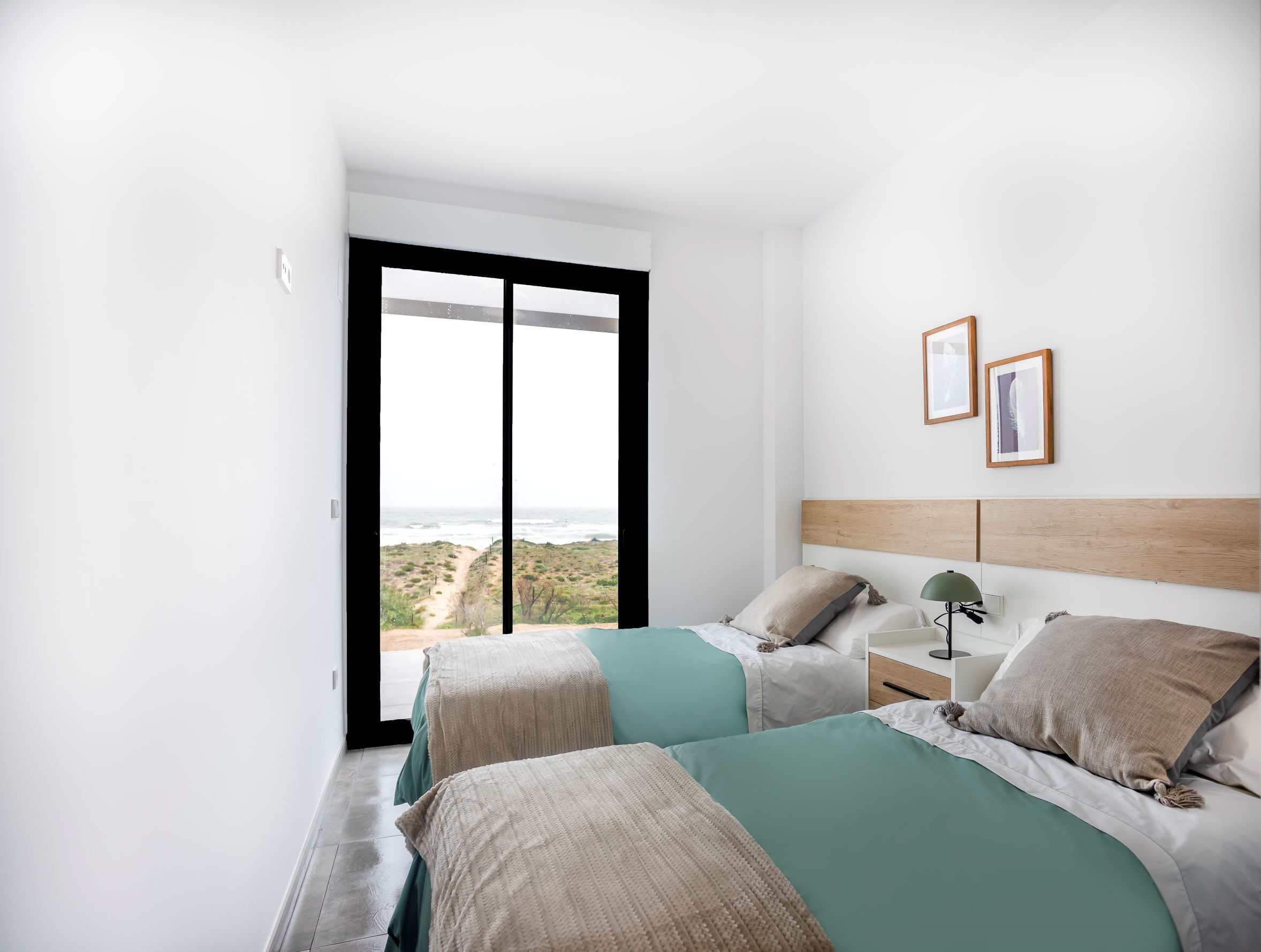 A bedroom with two beds, a nightstand, a lamp, and framed pictures on the wall.