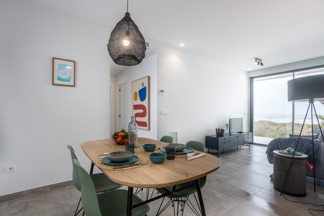 A modern dining area with a wooden table, green chairs, and a hanging light fixture.