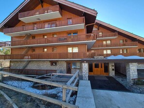A multi-story wooden building with balconies, a stone entrance, and a ski lift visible in the foreground. - Functional Apt near slopes, shops, with balcony & WiFi in Méribel (Méribel)