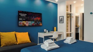 Habitación de hotel con cama, escritorio, silla y televisor mostrando una serie de Netflix.