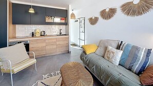 A modern kitchen with dark cabinets, a wooden countertop, and a built-in sink. There is a dining area with a white chair and a sofa with patterned cushions. - Bright T2 Apartment at the Old Port, La Ciotat (La Ciotat)