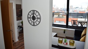 Ett modernt vardagsrum med ett stort fönster, en dekorativ väggklocka och en matplats med ett brickbord med drycker.