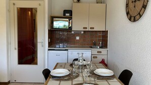 A compact kitchen with a microwave, sink, and dishwasher. A dining table is set with plates, glasses, and cutlery.