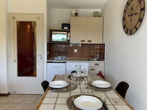Cozinha compacta com micro-ondas, pia e lava-louças. Uma mesa de jantar está posta com pratos, copos e talheres.