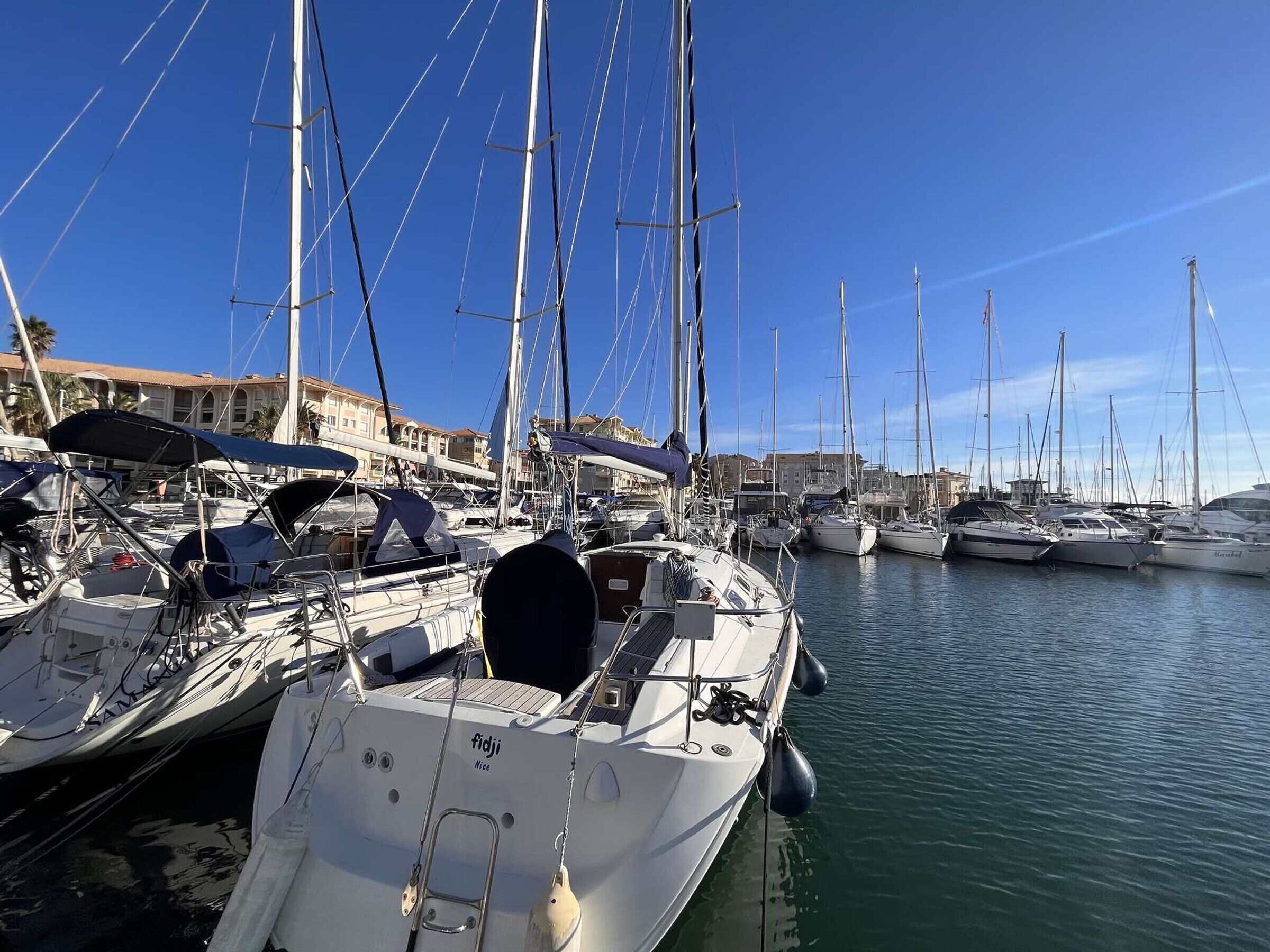 A marina with multiple sailboats docked, featuring a clear sky and calm water.