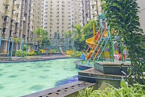 A swimming pool with a slide and play structures, surrounded by greenery and tall residential buildings. - Capital O 93455 Apartement Gateway Cicadas By Az Pro Ii (Bandung)
